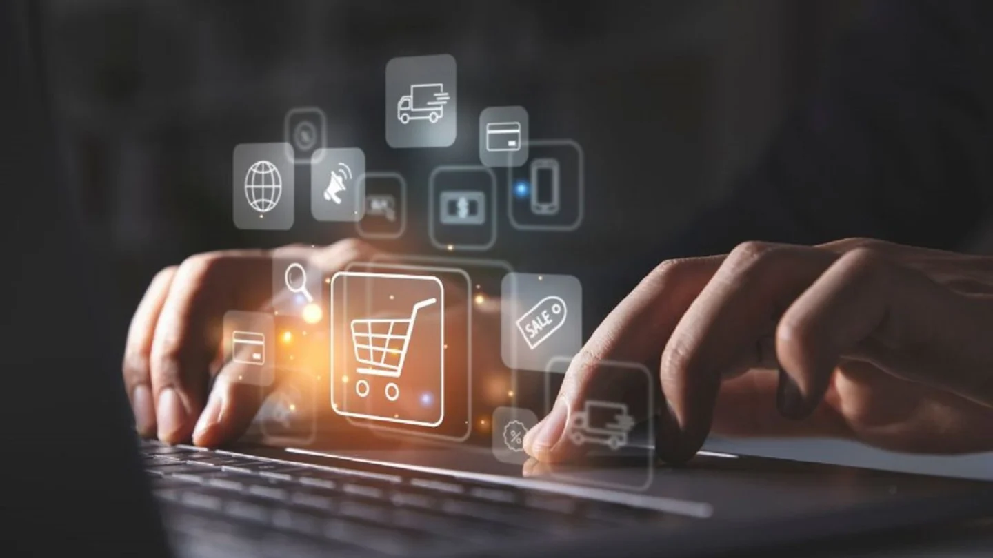 Hands at a laptop with glowing cart, payment and delivery icons above the keys, representing e-commerce development at Growth Yogi